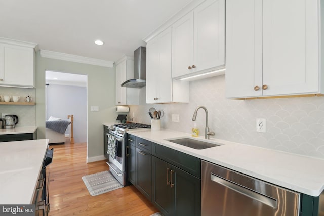 kitchen with wall chimney exhaust hood, stainless steel appliances, white cabinets, and a sink