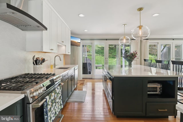 kitchen with light countertops, a sink, appliances with stainless steel finishes, and wall chimney range hood