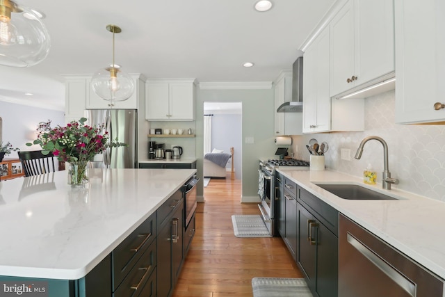 kitchen featuring wall chimney range hood, wood finished floors, a sink, white cabinets, and appliances with stainless steel finishes