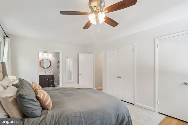 bedroom featuring ceiling fan, light wood-type flooring, ensuite bathroom, and a sink