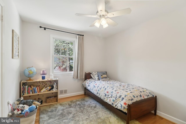 bedroom featuring baseboards, a ceiling fan, wood finished floors, and visible vents