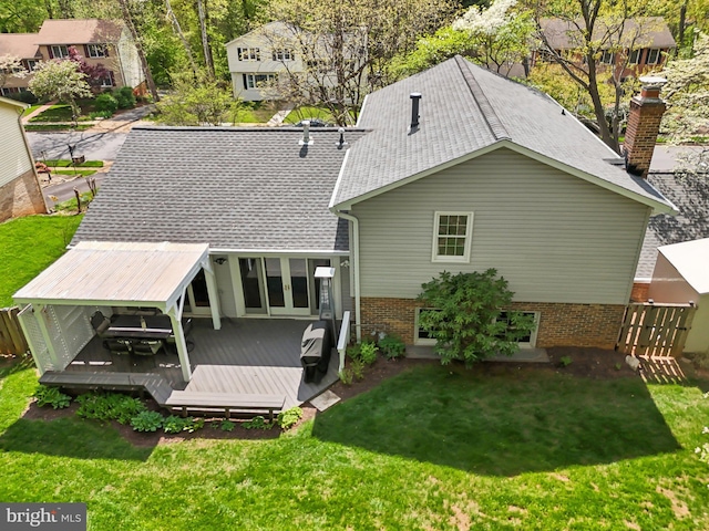 rear view of property featuring a chimney, brick siding, a shingled roof, a deck, and a yard