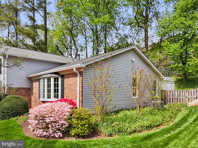 view of home's exterior with fence, brick siding, and roof with shingles