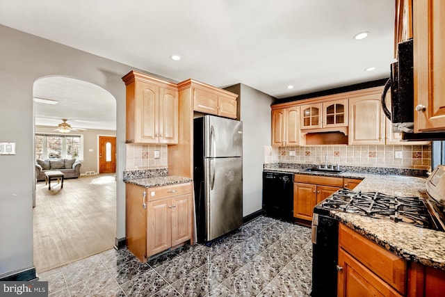 kitchen with arched walkways, black appliances, light stone counters, and a sink