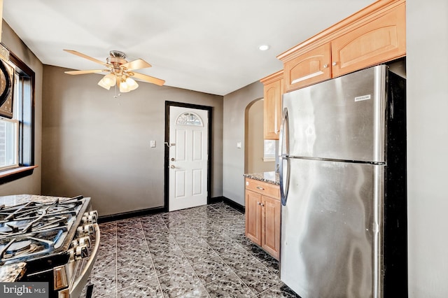 kitchen featuring light brown cabinets, baseboards, light stone countertops, arched walkways, and stainless steel appliances