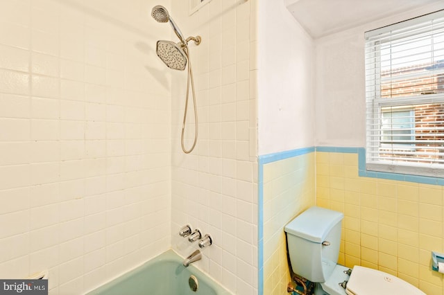 full bath with tile walls, a wainscoted wall, toilet, and bathing tub / shower combination