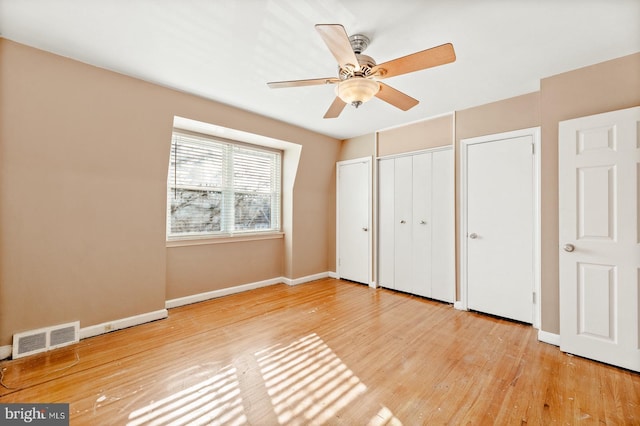 unfurnished bedroom featuring visible vents, multiple closets, baseboards, wood finished floors, and a ceiling fan