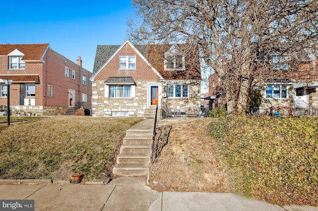 view of front facade featuring stone siding, brick siding, roof with shingles, and a front yard