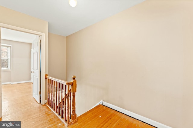 corridor with an upstairs landing, light wood-type flooring, and baseboards