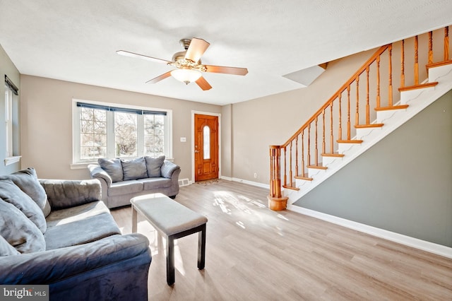 living room with stairway, light wood-style flooring, baseboards, and ceiling fan