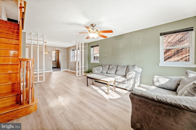 living room featuring a ceiling fan, light wood-style flooring, arched walkways, and baseboards