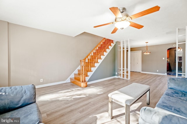 living area with baseboards, stairway, wood finished floors, arched walkways, and a ceiling fan