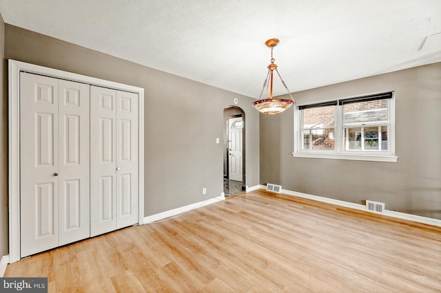 unfurnished dining area featuring arched walkways, visible vents, baseboards, and wood finished floors