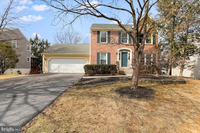 colonial home featuring aphalt driveway, brick siding, and a garage