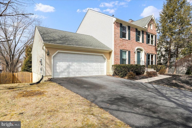 colonial home featuring driveway, fence, an attached garage, brick siding, and a chimney