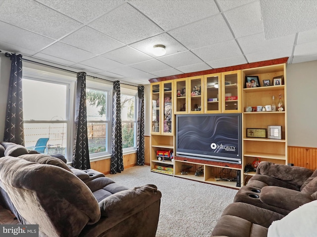 living area featuring carpet flooring, a paneled ceiling, wooden walls, and a wainscoted wall