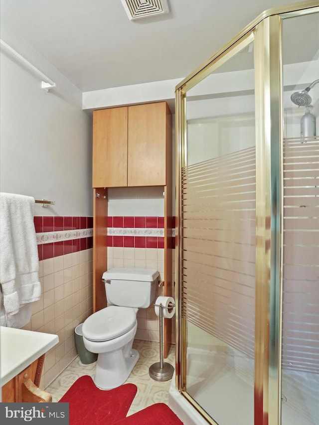 bathroom featuring visible vents, toilet, wainscoting, a stall shower, and tile walls