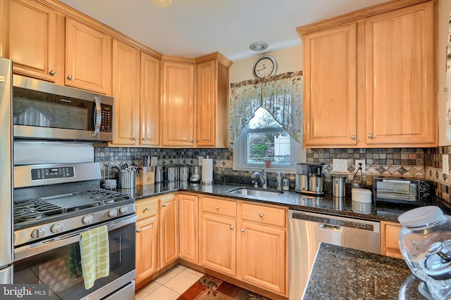 kitchen featuring light tile patterned floors, decorative backsplash, dark stone countertops, appliances with stainless steel finishes, and a sink