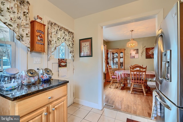 kitchen featuring visible vents, baseboards, light tile patterned floors, dark stone countertops, and stainless steel fridge