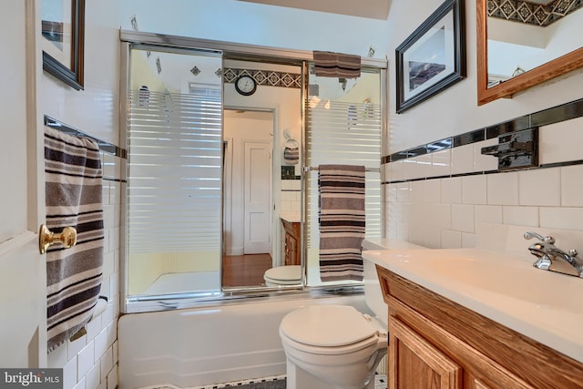 bathroom featuring vanity, tile walls, toilet, and bath / shower combo with glass door