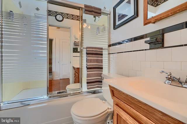 full bathroom with vanity, tile walls, toilet, and a shower with shower door