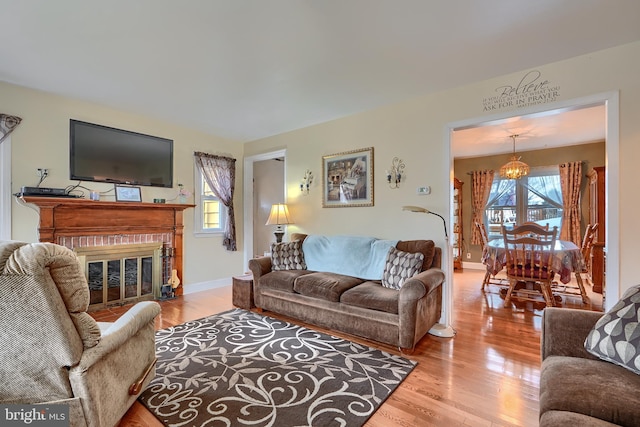 living room featuring a fireplace, baseboards, an inviting chandelier, and wood finished floors