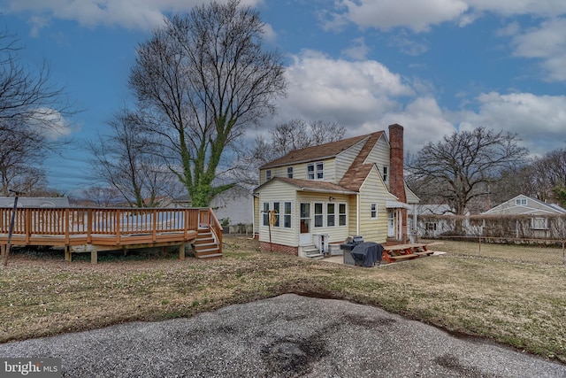 rear view of property with a wooden deck, a lawn, entry steps, and a chimney