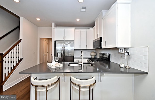 kitchen with visible vents, dark wood finished floors, a peninsula, a sink, and appliances with stainless steel finishes