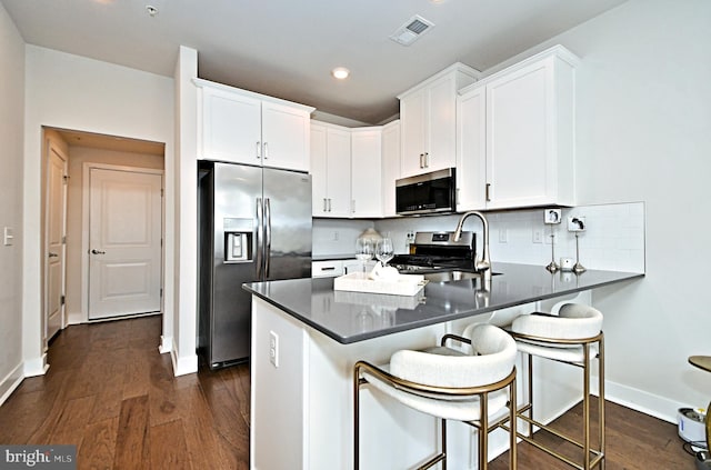 kitchen with decorative backsplash, a peninsula, dark wood finished floors, and appliances with stainless steel finishes