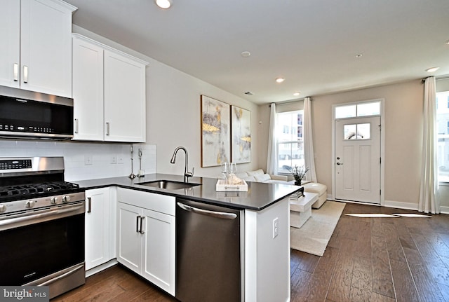 kitchen with a sink, dark countertops, dark wood-style floors, appliances with stainless steel finishes, and a peninsula