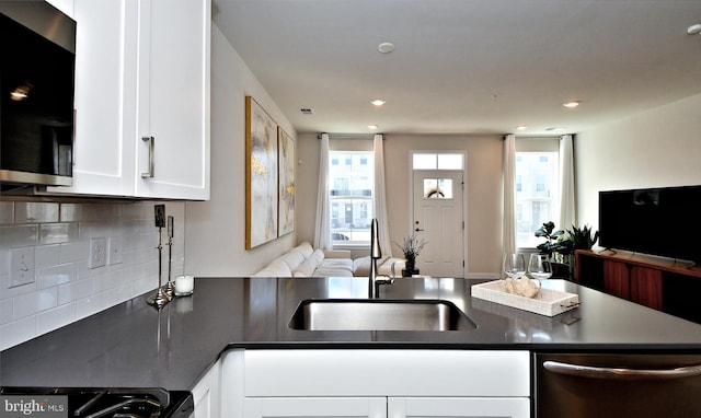 kitchen featuring dark countertops, a sink, open floor plan, white cabinetry, and stainless steel dishwasher