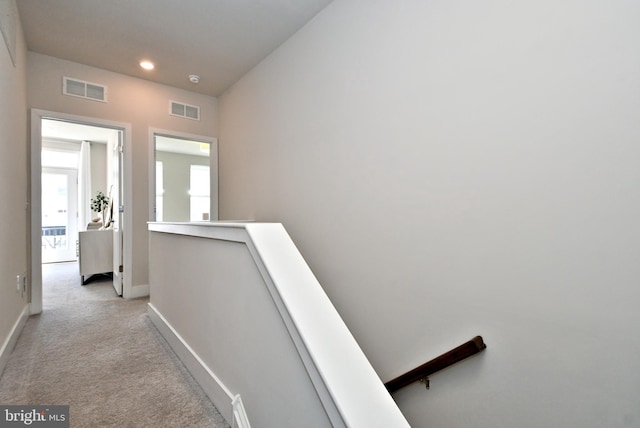 corridor with visible vents, an upstairs landing, light colored carpet, and baseboards