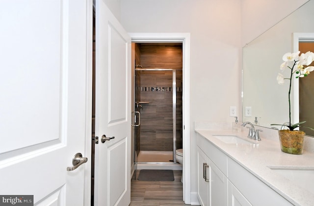 bathroom with wood finished floors, double vanity, a stall shower, a sink, and toilet