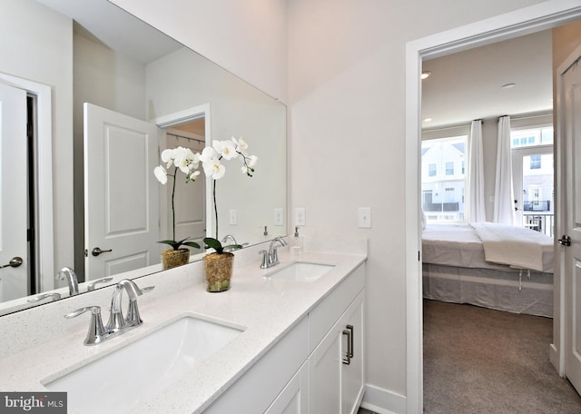 bathroom with double vanity, connected bathroom, baseboards, and a sink