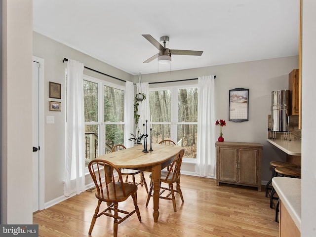 dining area with light wood-style flooring, a ceiling fan, and baseboards