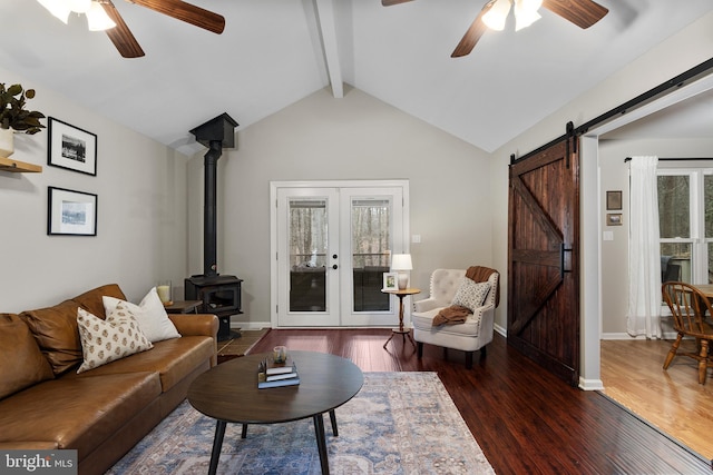 living area with lofted ceiling with beams, wood finished floors, a barn door, french doors, and a wood stove