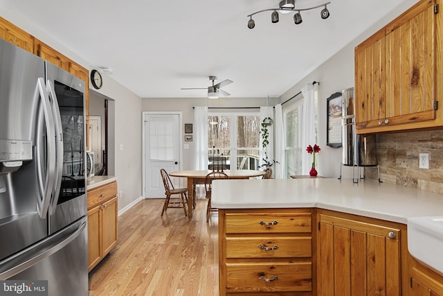 kitchen featuring backsplash, light countertops, a peninsula, light wood-style floors, and stainless steel refrigerator with ice dispenser