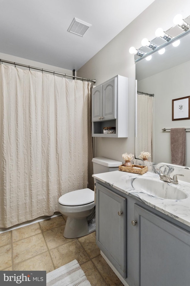 bathroom featuring vanity, stone tile floors, toilet, and visible vents