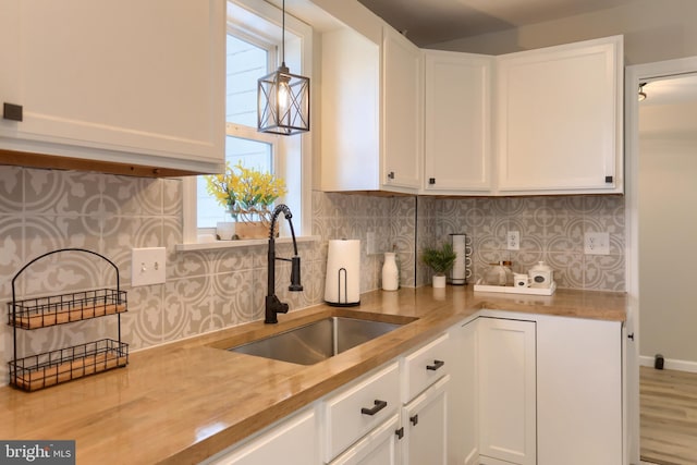 kitchen featuring a sink, decorative backsplash, pendant lighting, and white cabinets