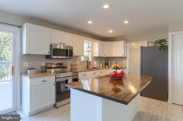 kitchen featuring light wood-style flooring, a sink, backsplash, appliances with stainless steel finishes, and white cabinets