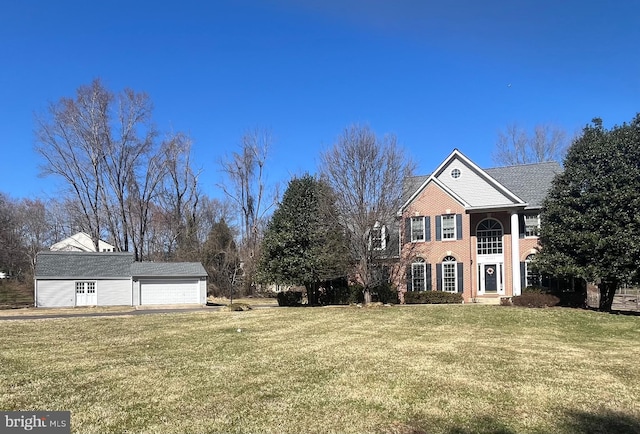 view of front facade featuring a detached garage, brick siding, an outbuilding, and a front yard