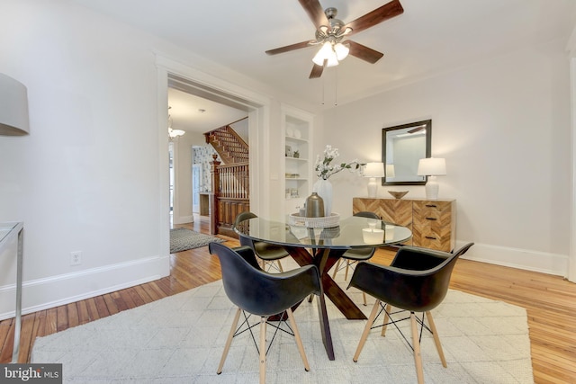 dining space featuring built in features, wood finished floors, baseboards, a ceiling fan, and stairs