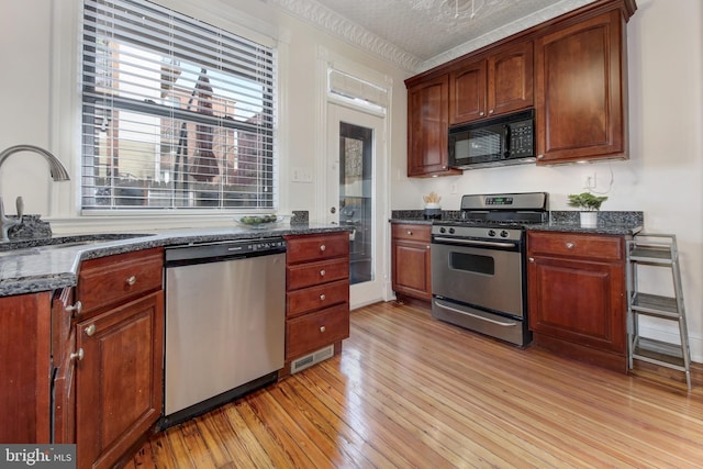 kitchen with dark stone counters, a sink, appliances with stainless steel finishes, a textured ceiling, and light wood-type flooring