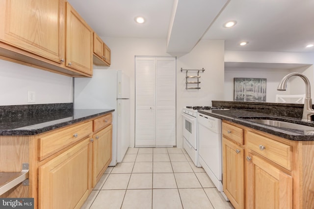 kitchen with dark stone countertops, white appliances, light tile patterned floors, light brown cabinets, and a sink