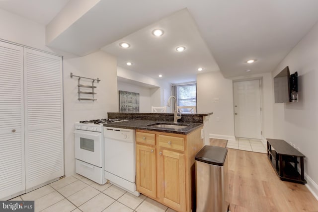 kitchen featuring recessed lighting, dark stone countertops, a peninsula, white appliances, and a sink