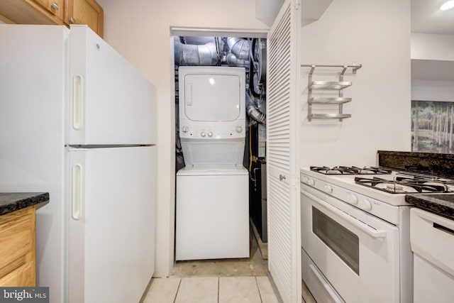 kitchen with dark countertops, stacked washer / dryer, white appliances, and light tile patterned flooring