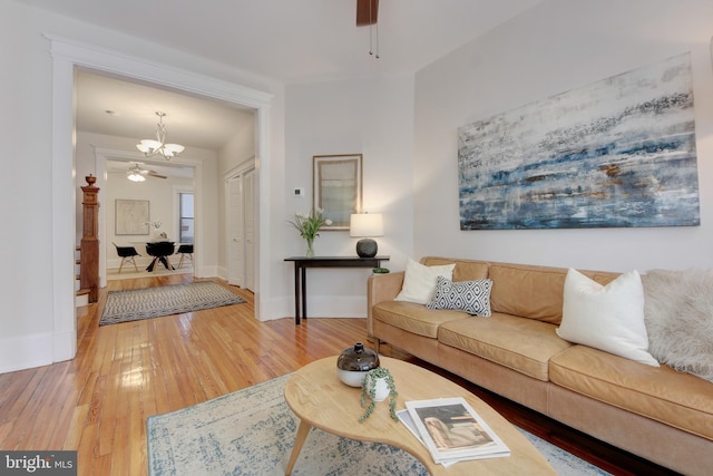 living area with light wood finished floors, ceiling fan with notable chandelier, and baseboards