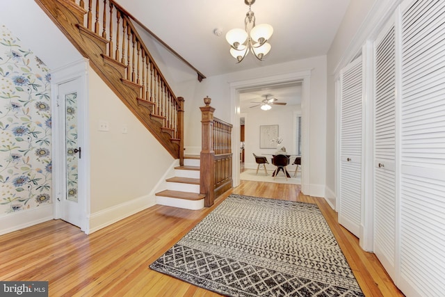 foyer featuring light wood-type flooring, baseboards, ceiling fan with notable chandelier, and stairway