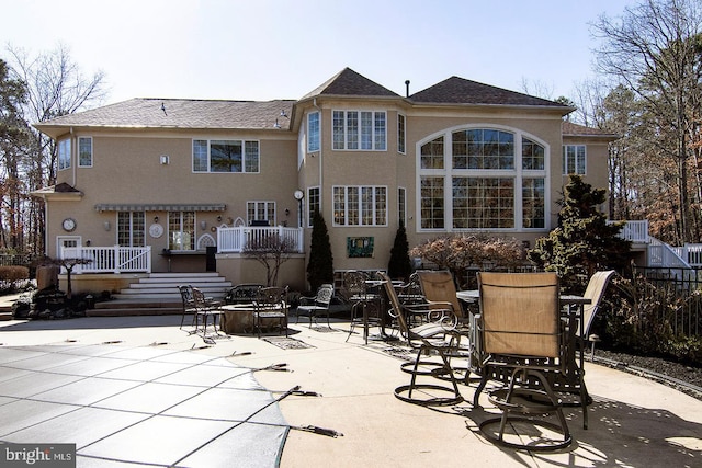 back of property featuring a patio, stucco siding, a wooden deck, and an outdoor fire pit