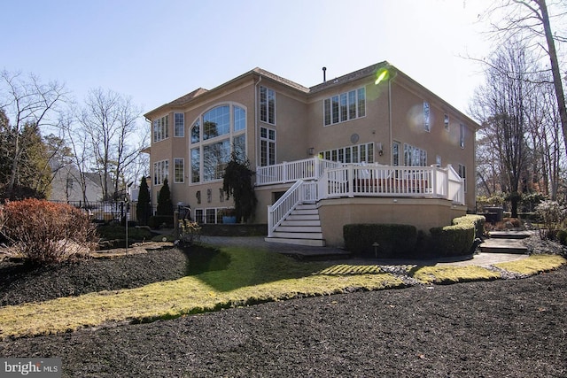 rear view of house with stairs, a wooden deck, and stucco siding